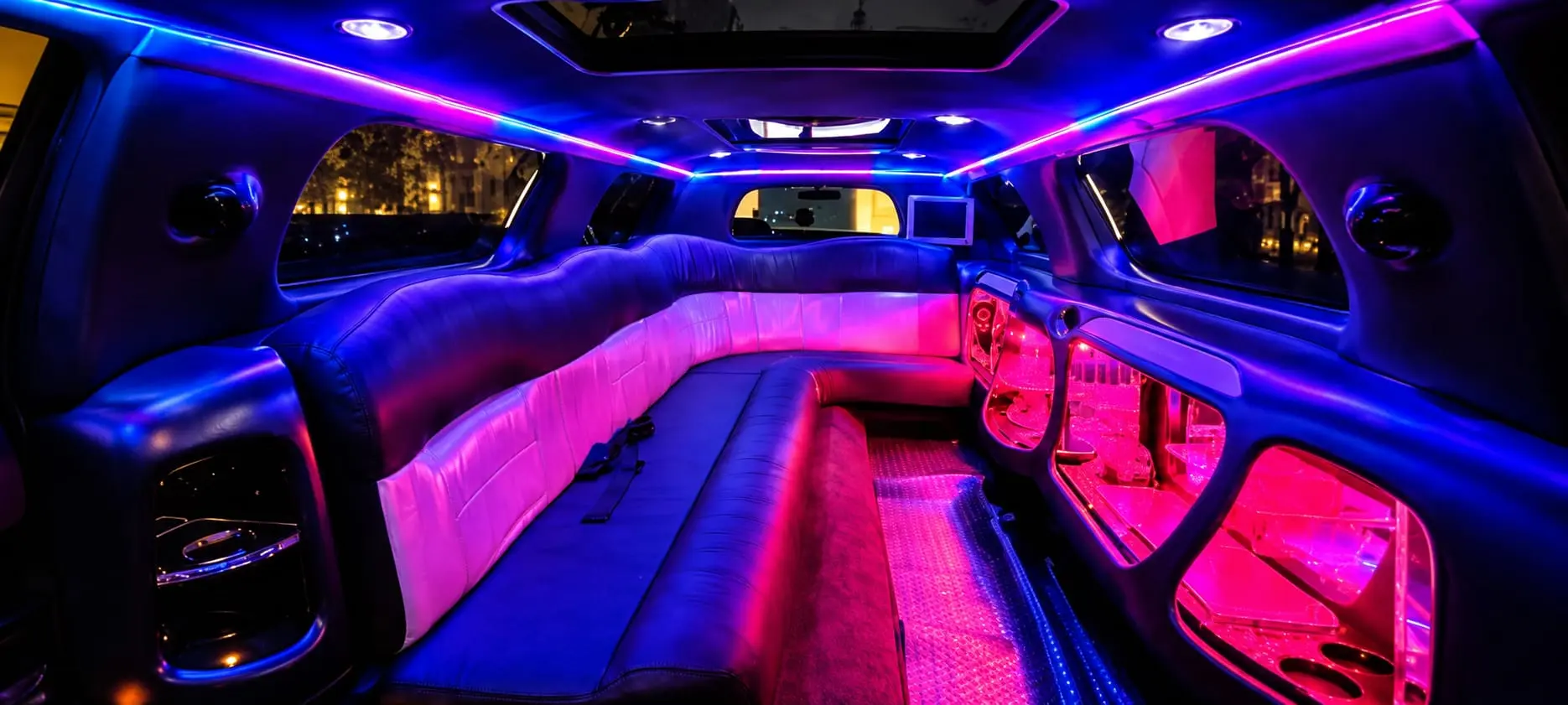 Interior de limusina de lujo con asientos de cuero y luces LED azules, violetas y rosas para fiestas y celebraciones.