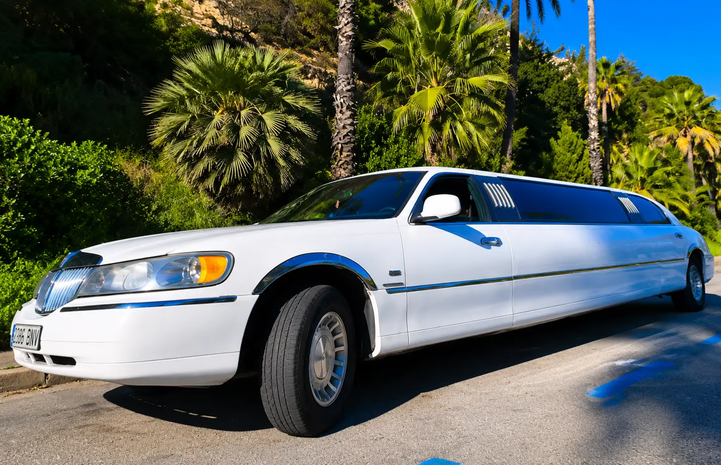 White Lincoln stretch limousine in Barcelona, Spain, featuring tinted windows, chrome accents, and a tropical-style landscape on a sunny day.